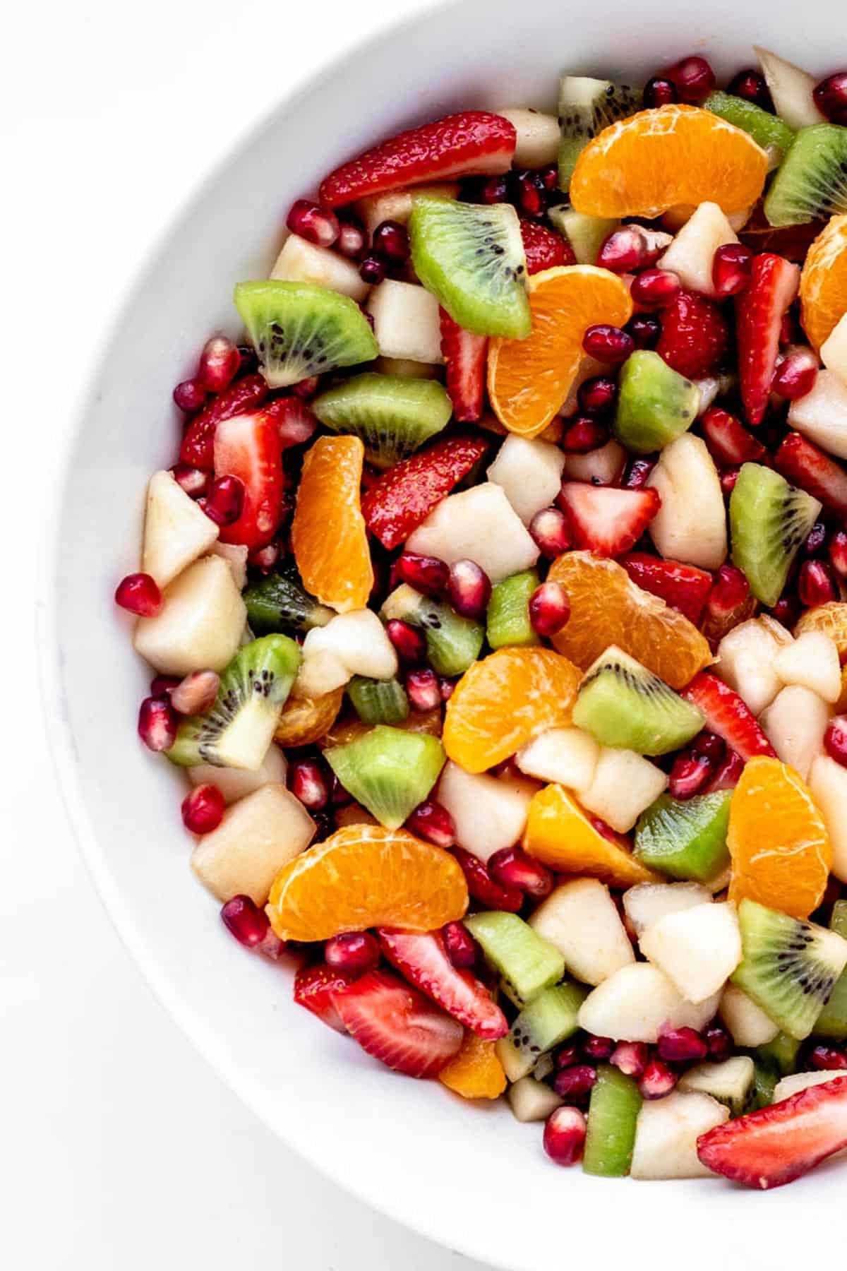 A closeup of Christmas fruit salad in a white serving bowl.