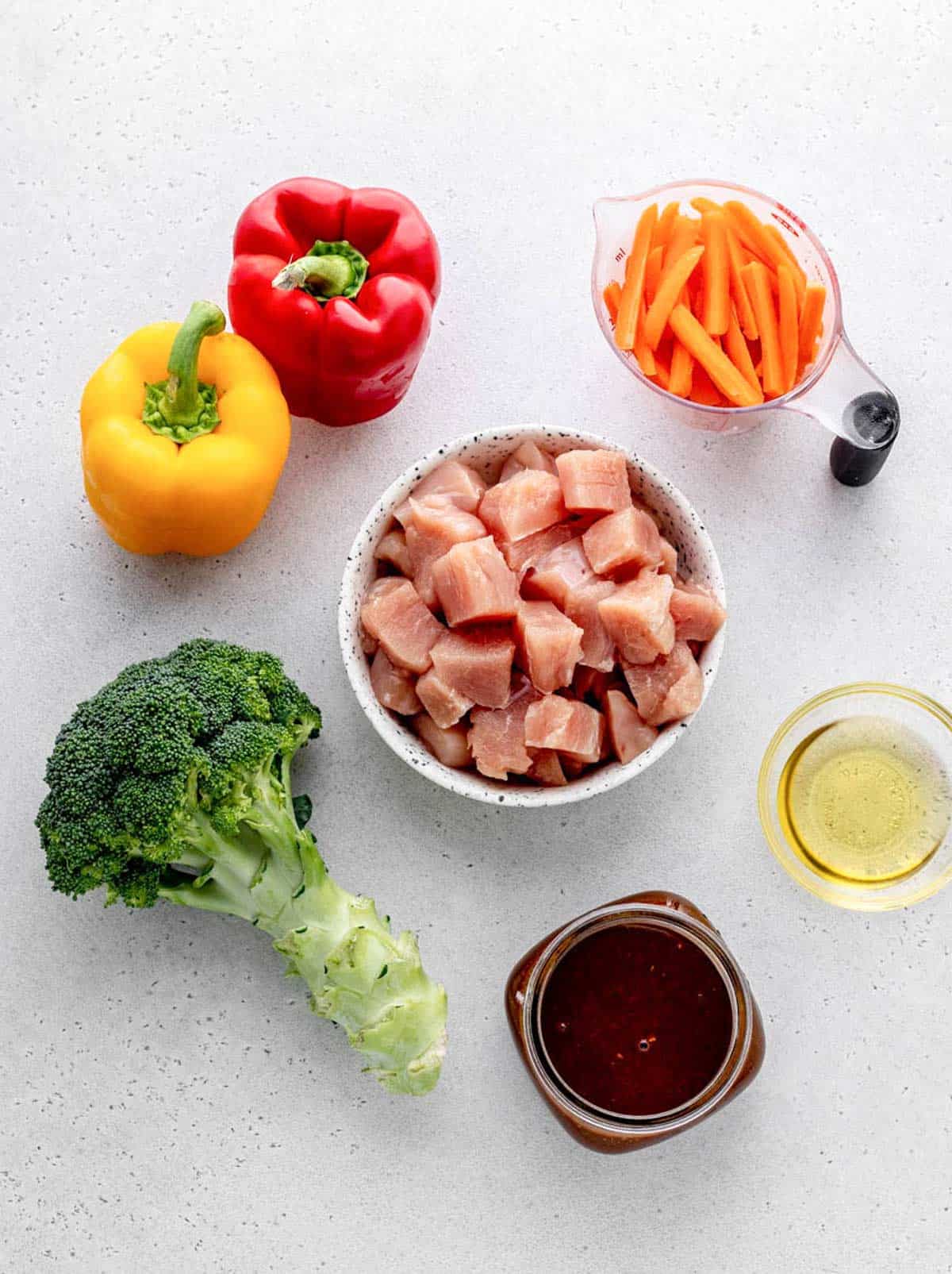 The ingredients for healthy chicken stir fry, including bell peppers, broccoli, chicken, stir fry sauce, sesame oil and baby carrots.