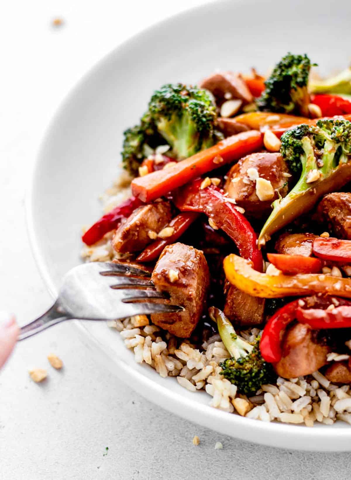 A fork poking into a bowl of healthy stir fry with chicken served over rice.