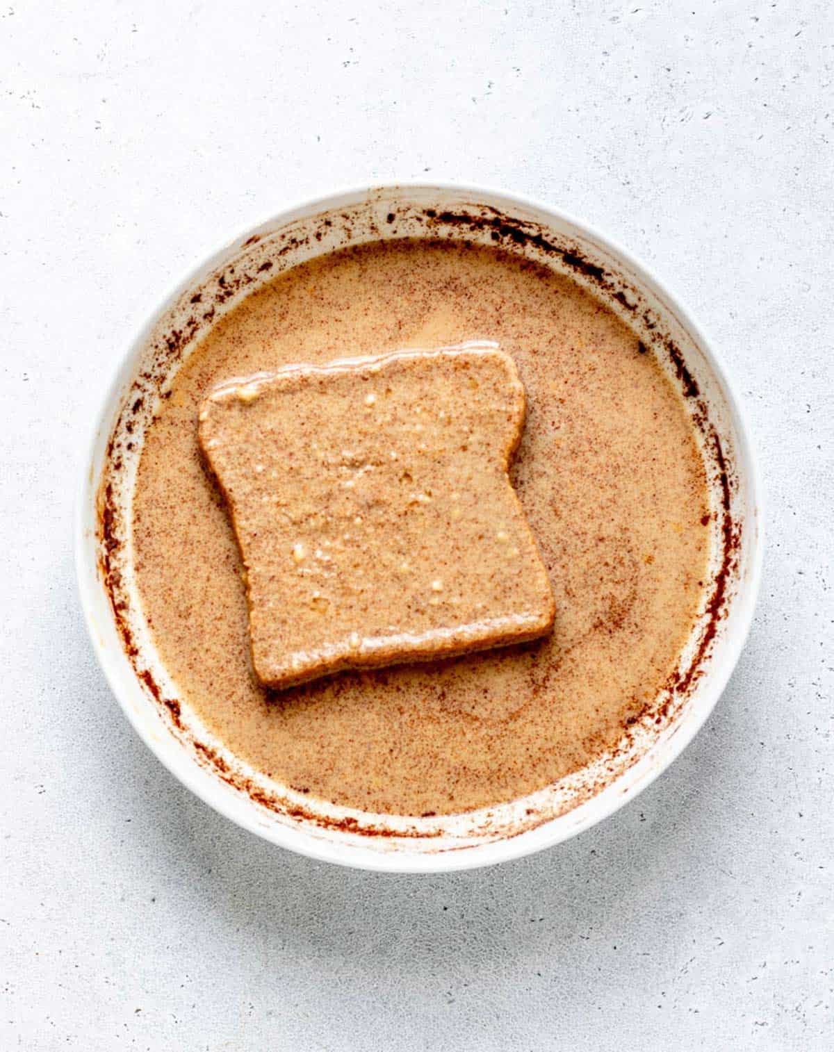 A piece of whole wheat Texas toast soaking in the healthy French toast batter.