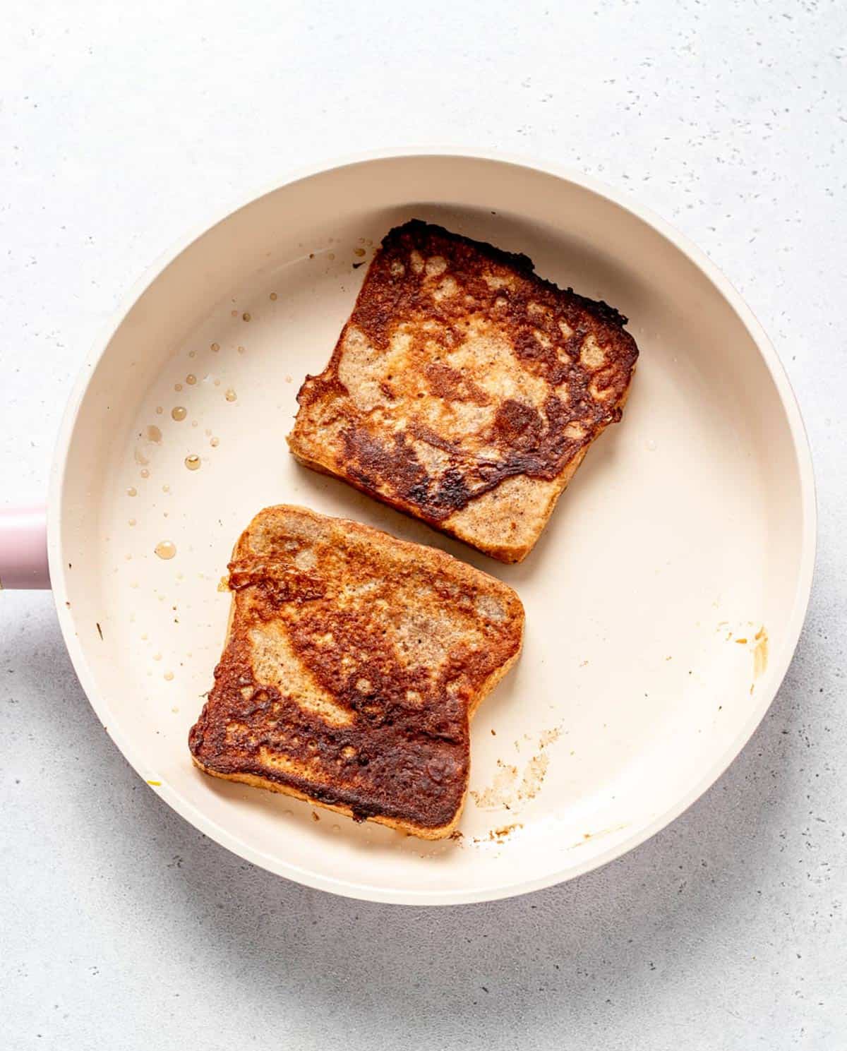 A non stick frying pan with two slices of high protein French toast frying in coconut oil.