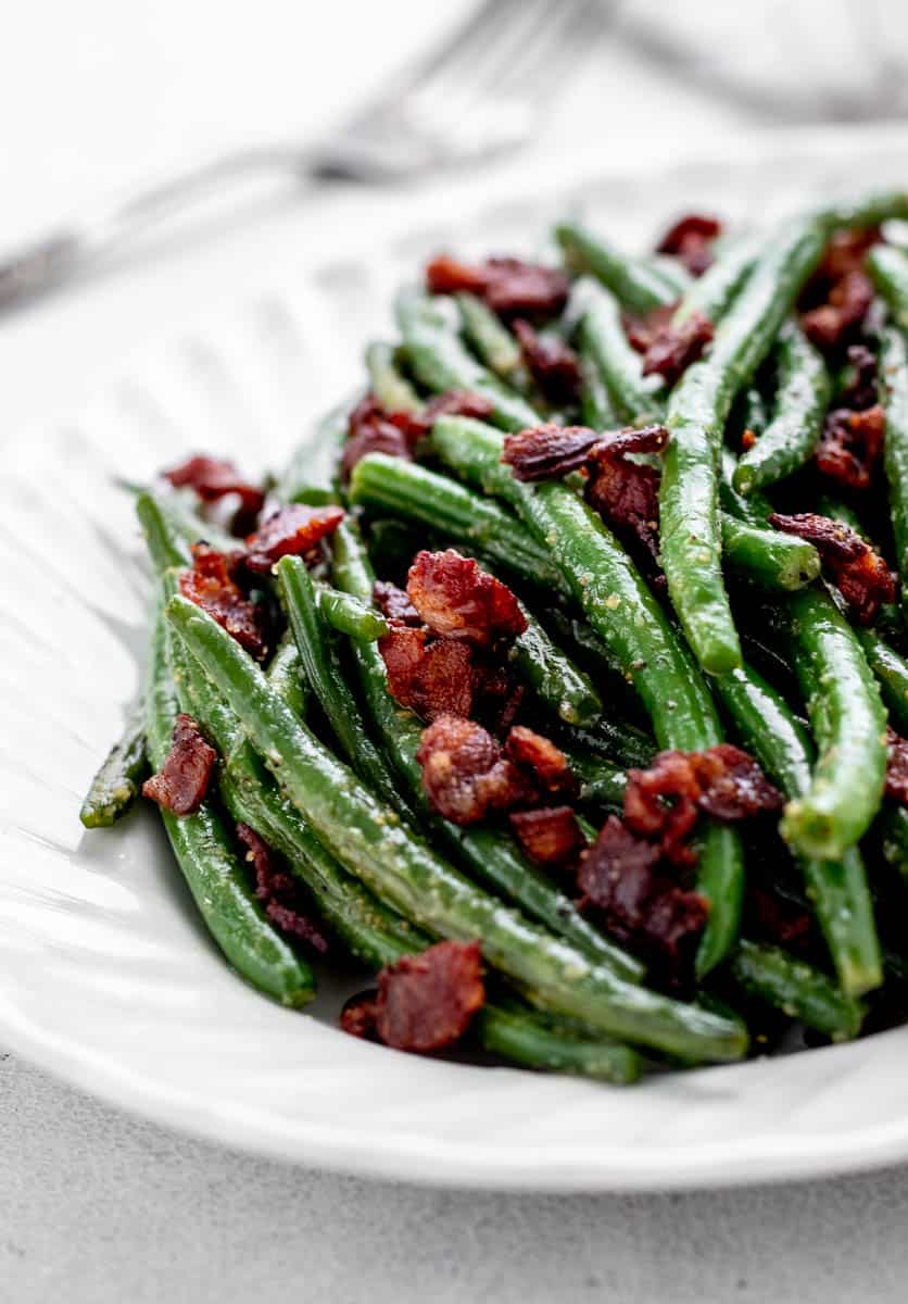 A closeup of seasoned green beans and bacon on a white plate.