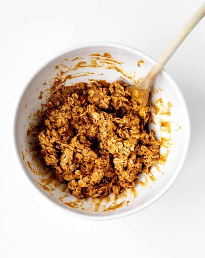 Ingredients mixed together for the peanut butter energy bites in a large white bowl with a wooden spoon.
