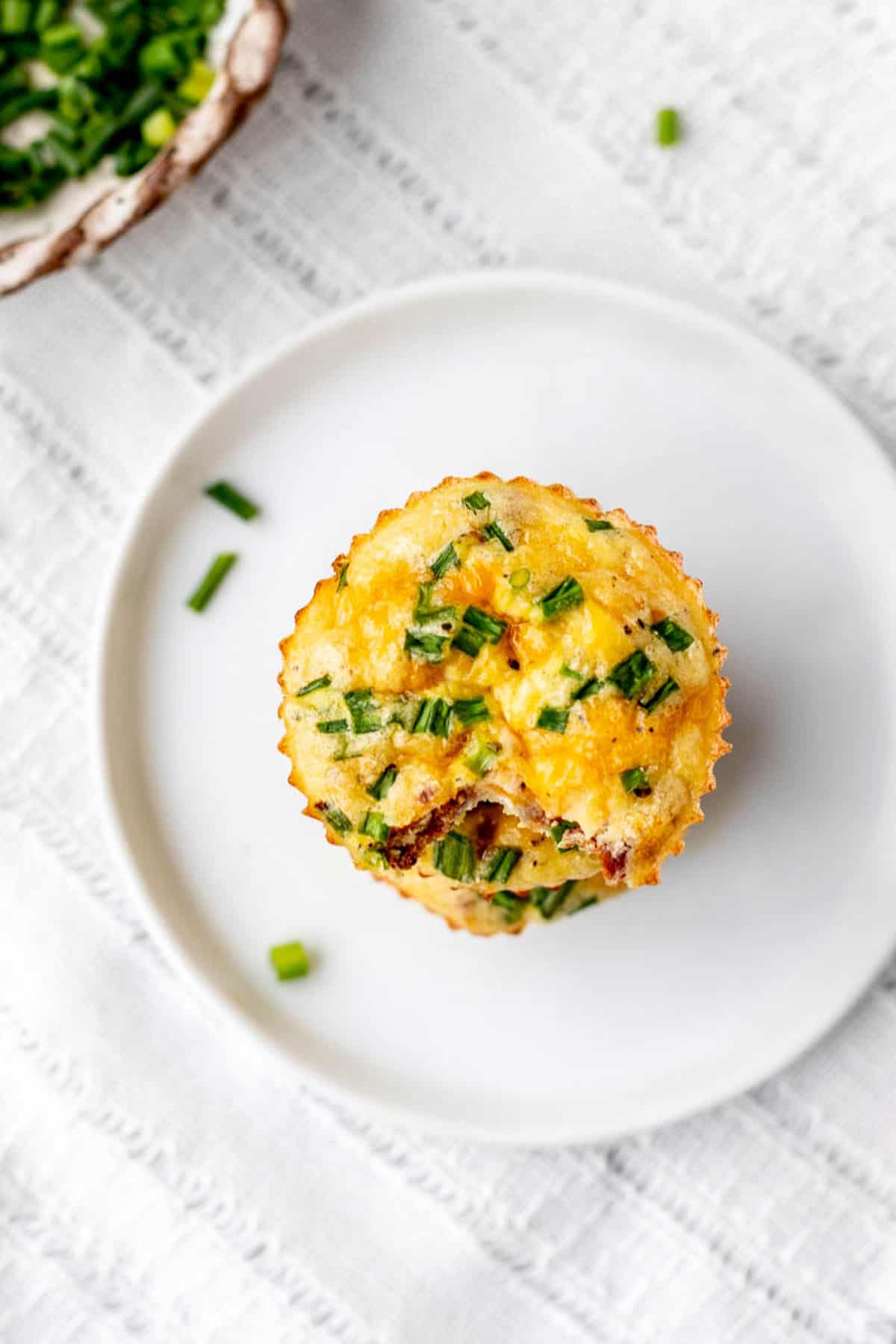 A top down view of a stack of mini crustless quiches on a white plate.