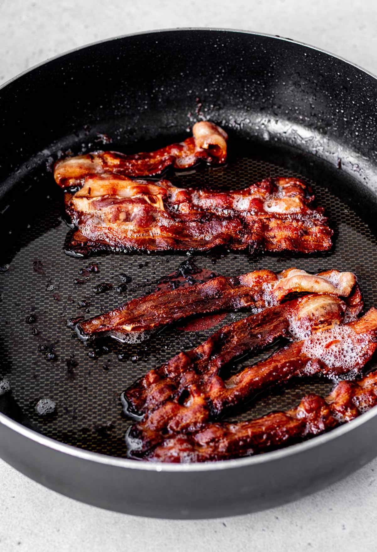 A large frying pan with crisp cooked bacon.