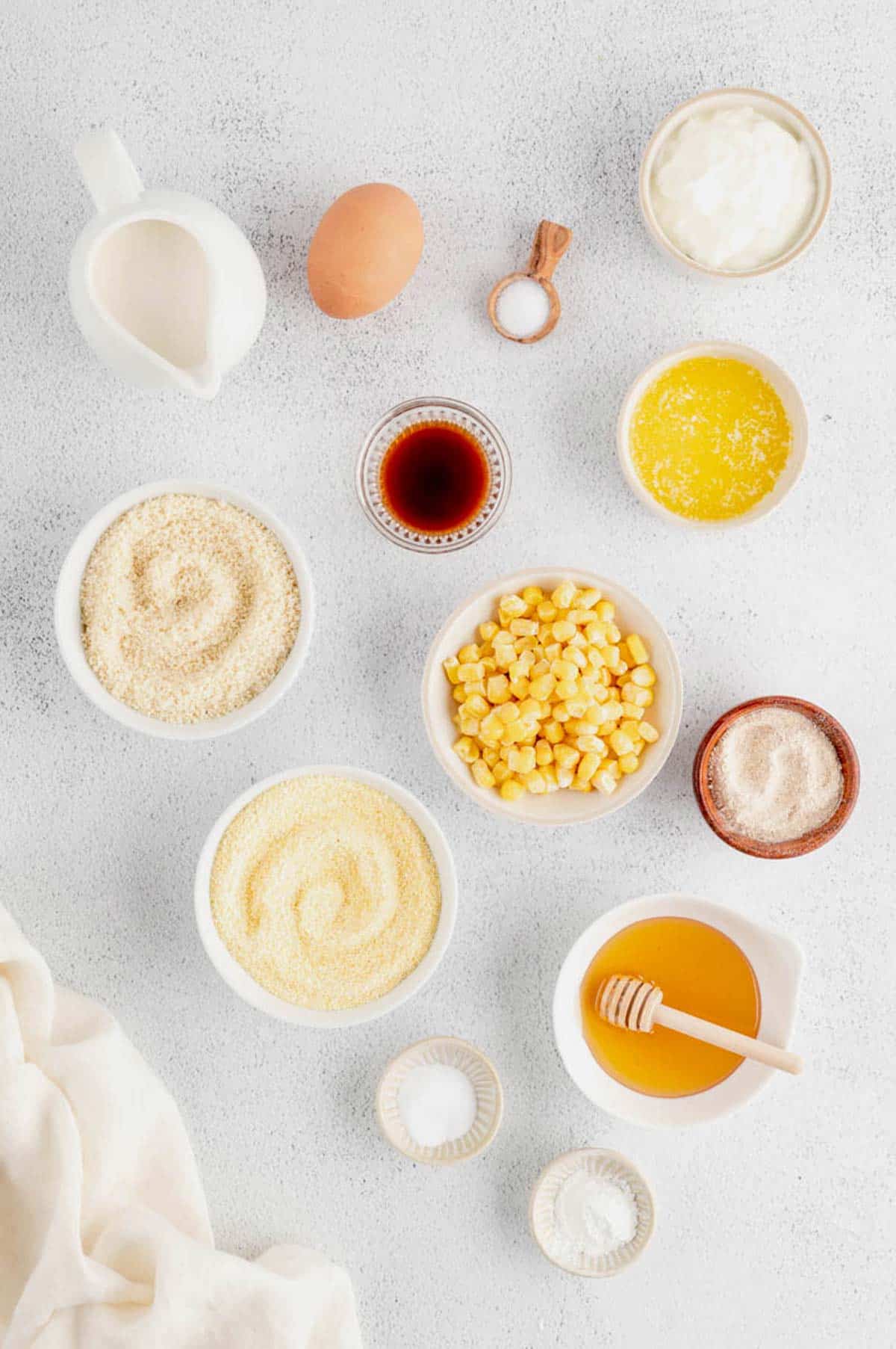 Ingredients for healthy cornbread recipe including almond milk, egg, coconut oil, Greek yogurt, cornmeal, flours, honey, vanilla and frozen corn kernels.