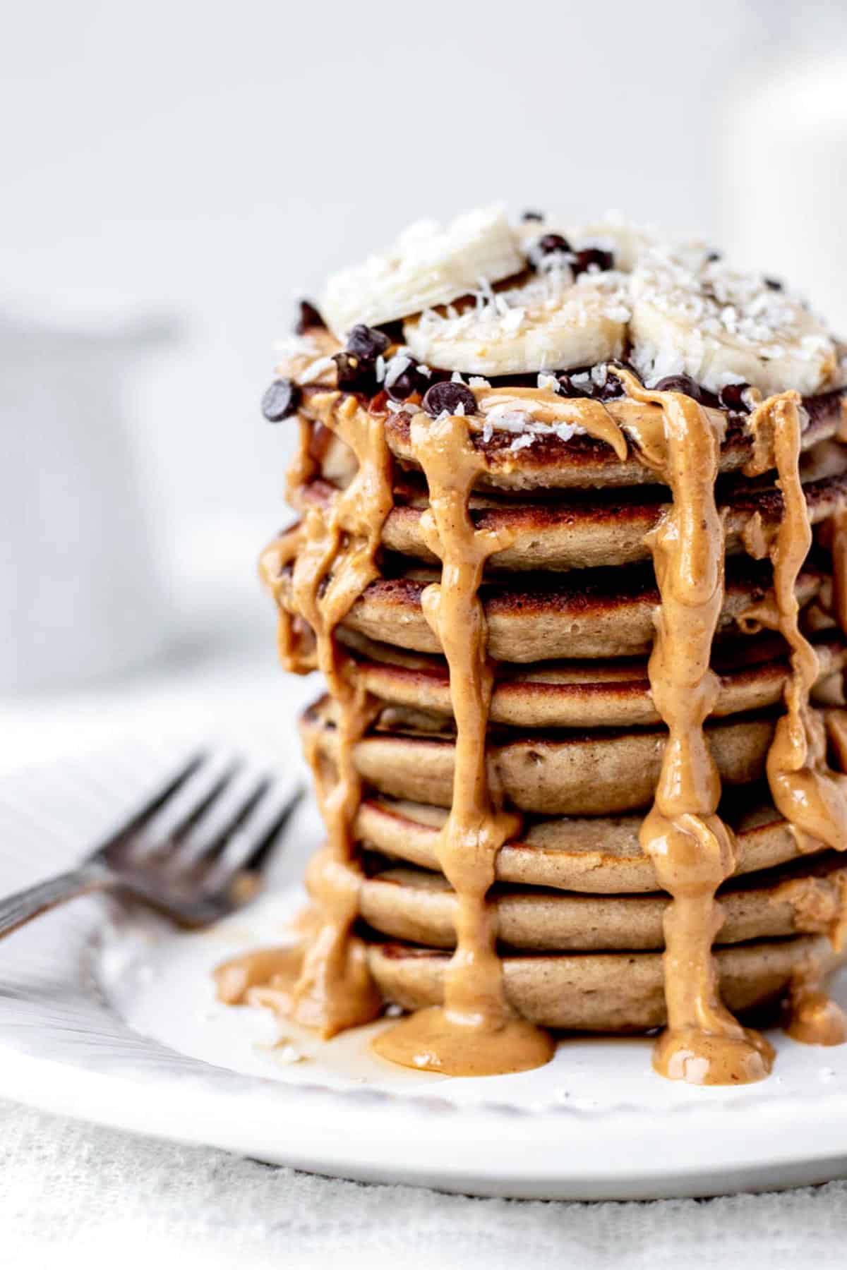 A big stack of protein pancakes topped with peanut butter, bananas, chocolate chips and shredded coconut.