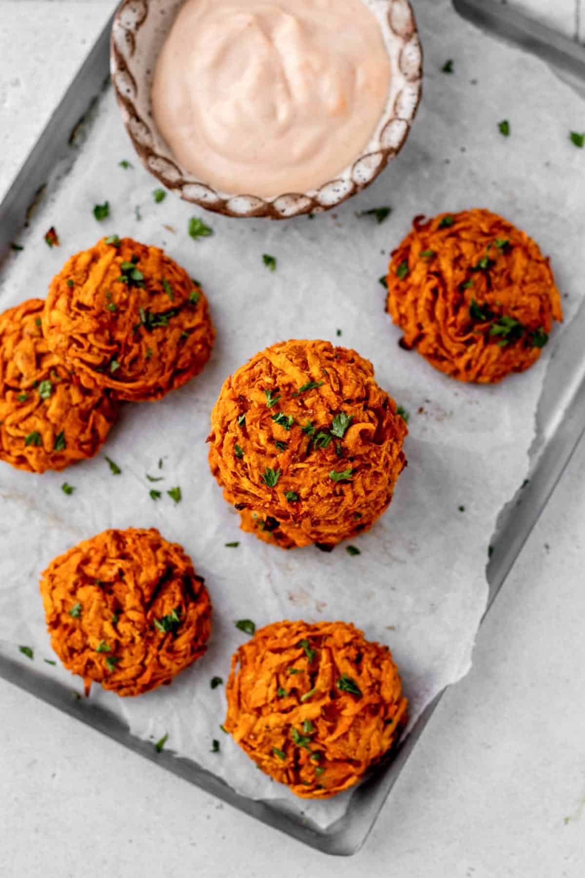 Baked sweet potato fritters and a small bowl of a creamy dipping sauce.