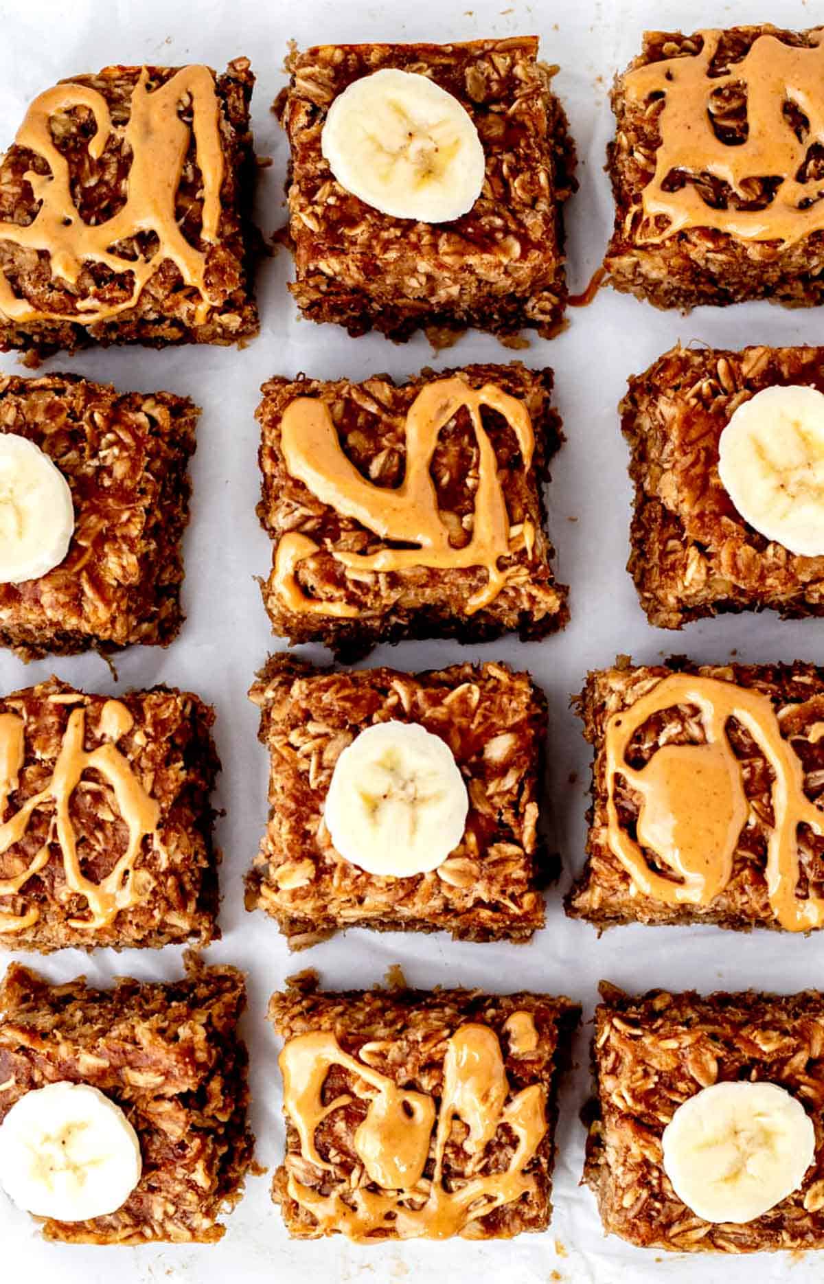 A close up image of sliced banana oat bars topped with peanut butter drizzle and banana slices. 