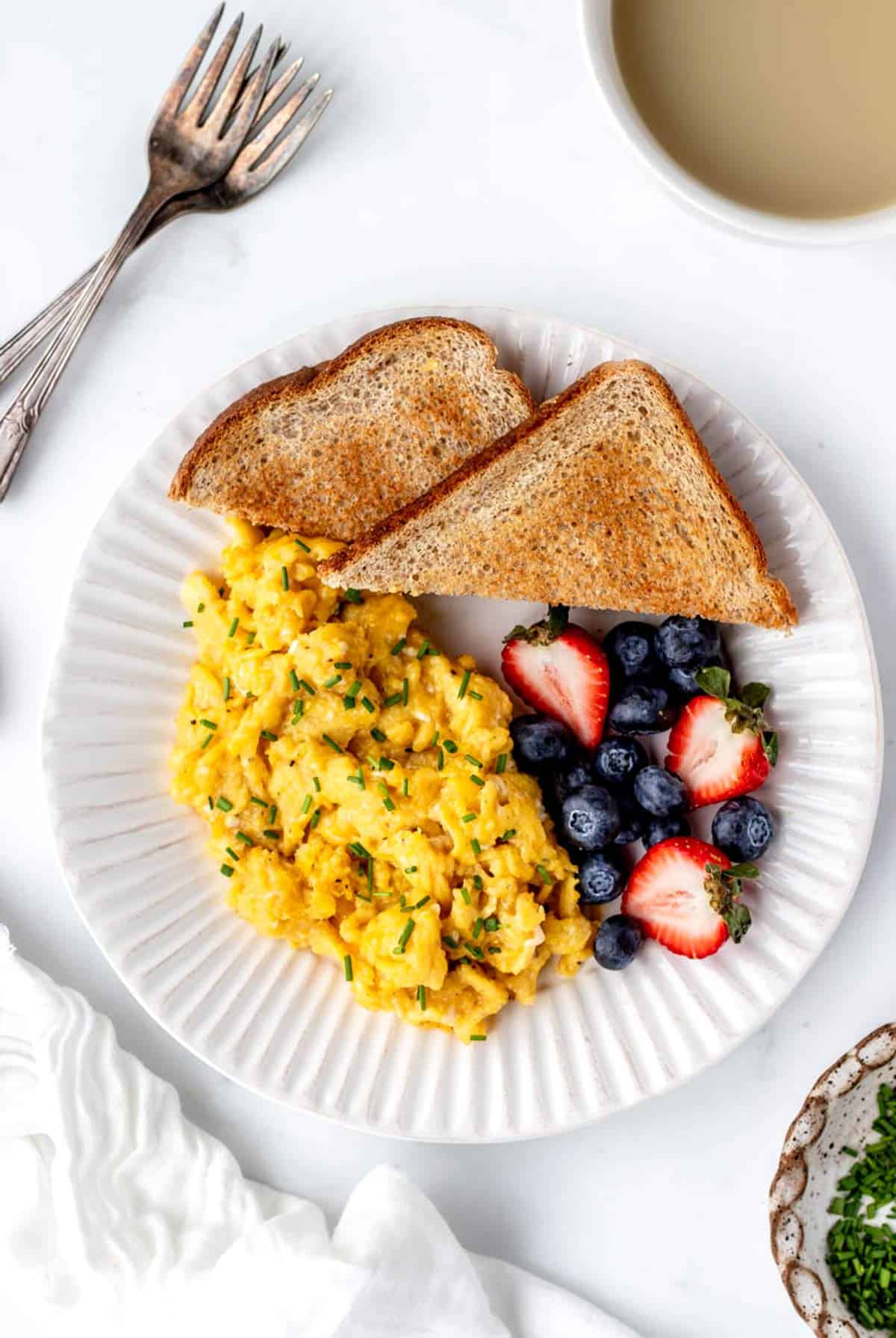 A top down view of soft scrambled eggs, fresh berries and toast on a white plate.