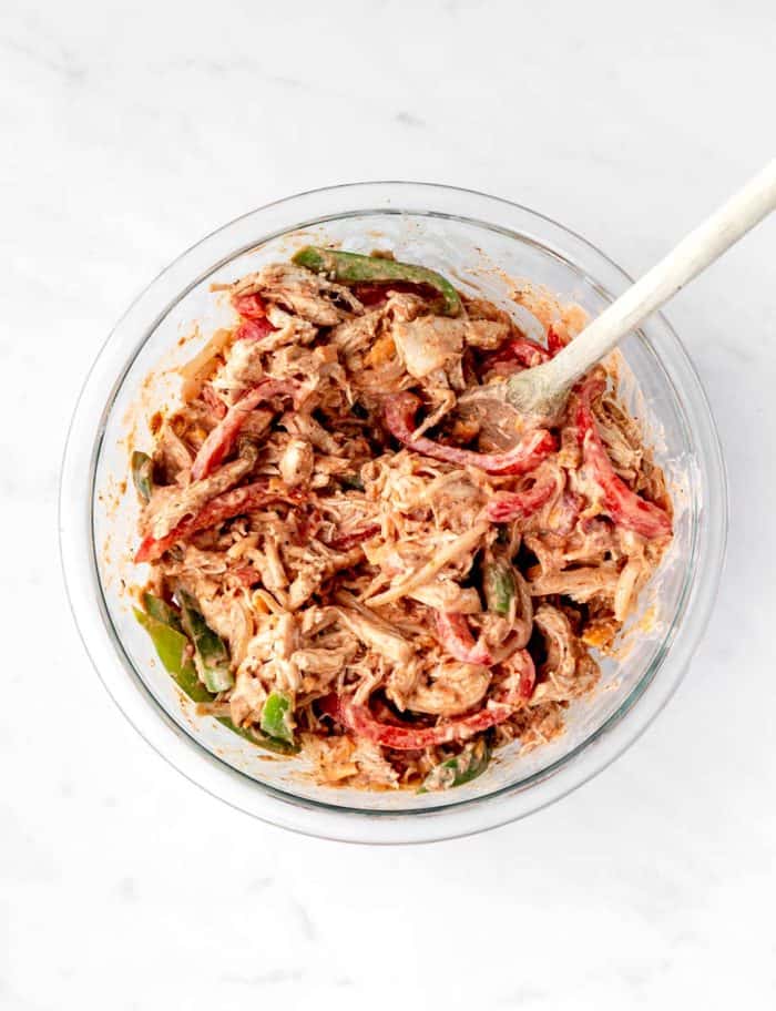 A large glass bowl of shredded chicken, red and green bell peppers, onion and cream cheese fajita mix.
