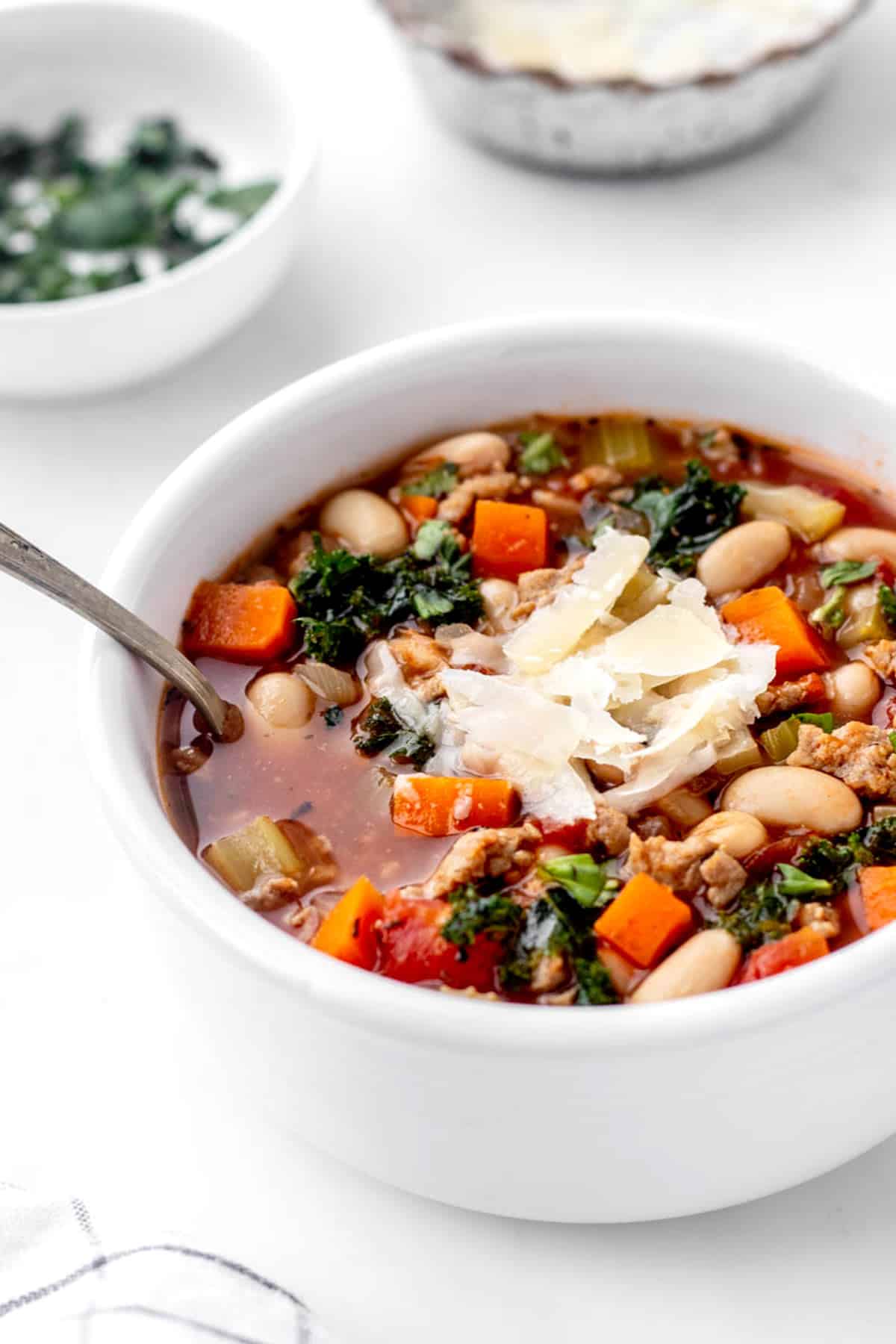 Healthy sausage and kale soup in a white bowl topped with fresh basil and parmesan cheese.