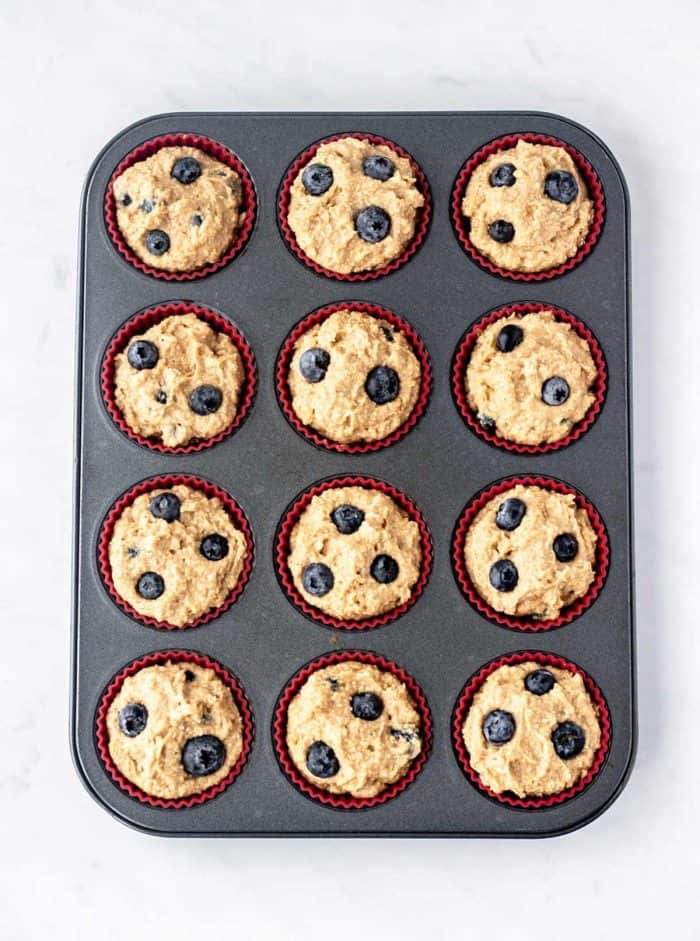 Twelve unbaked blueberry protein muffins in a muffin pan.