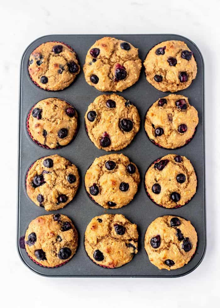 Twelve baked blueberry protein muffins in a muffin tin.