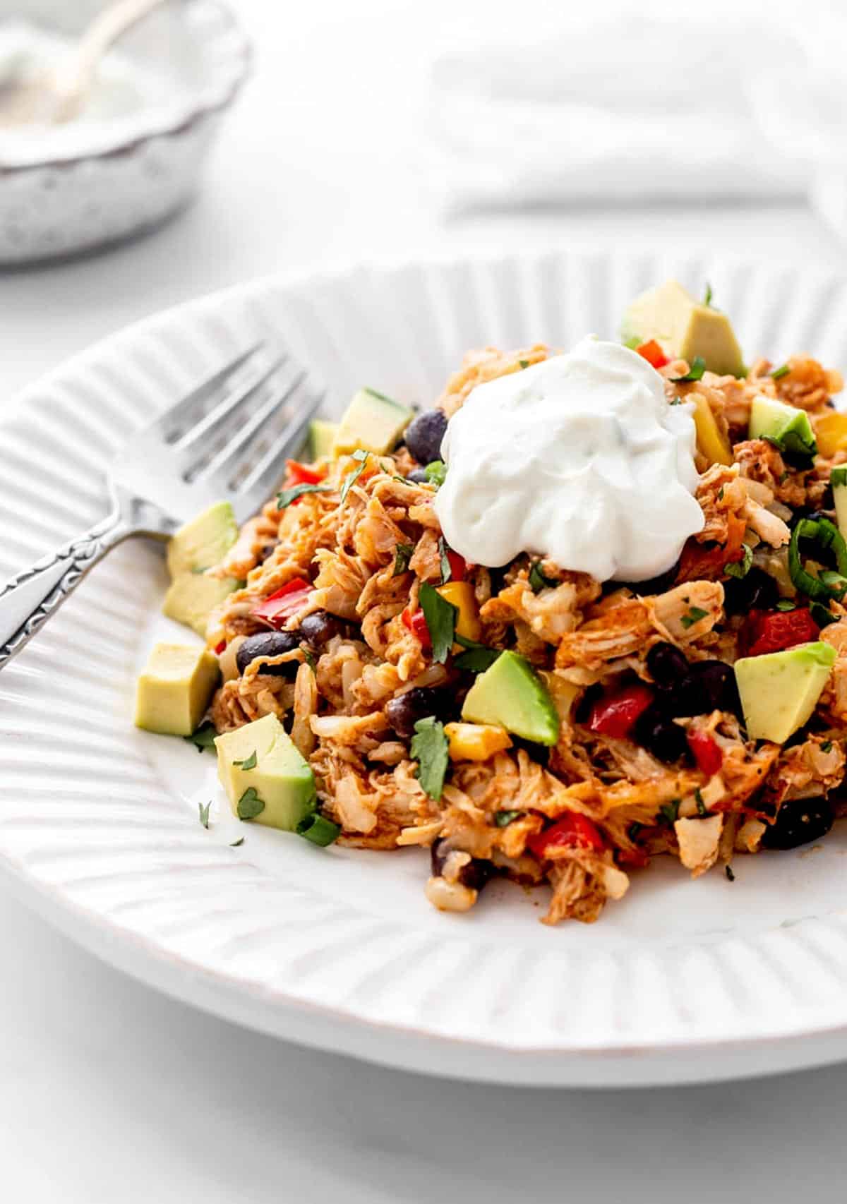 A helping of chicken burrito casserole on a plate with a dollop of Greek yogurt and diced avocado.