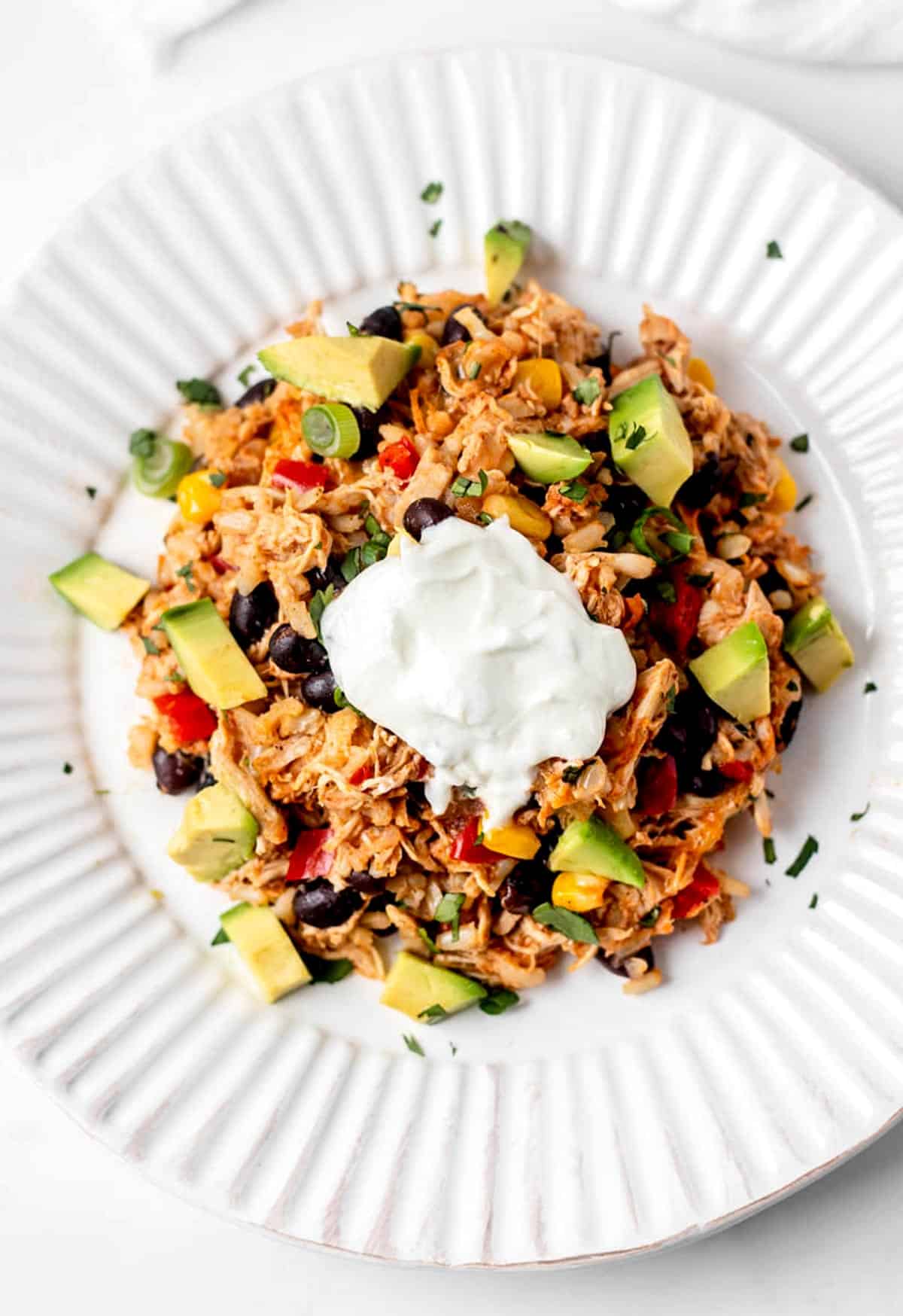 Shredded chicken burrito rice bowl topped with diced avocado and Greek yogurt.