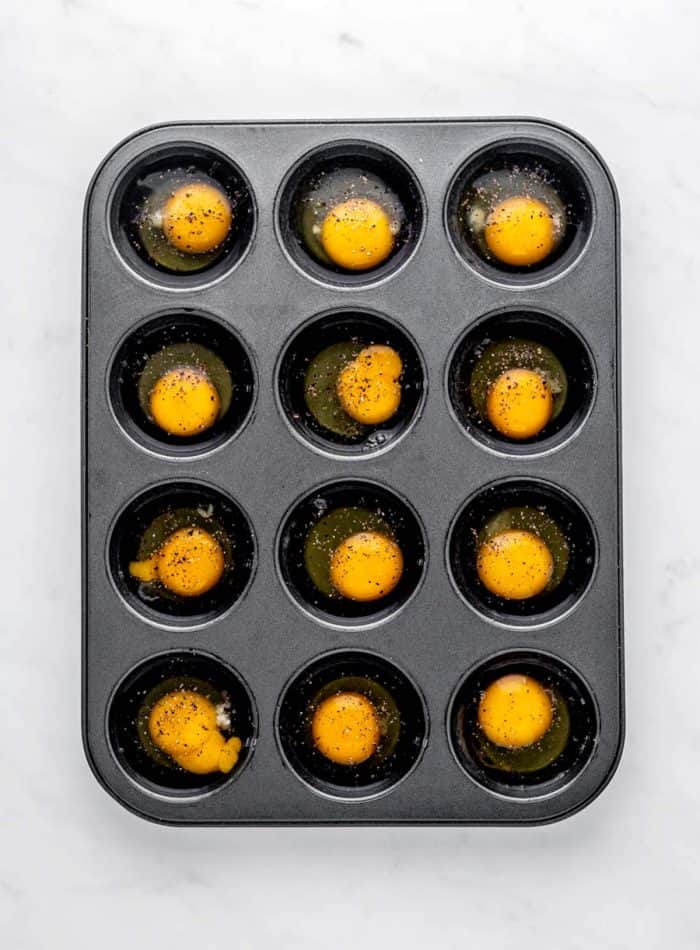 Twelve eggs cracked into a muffin tin.