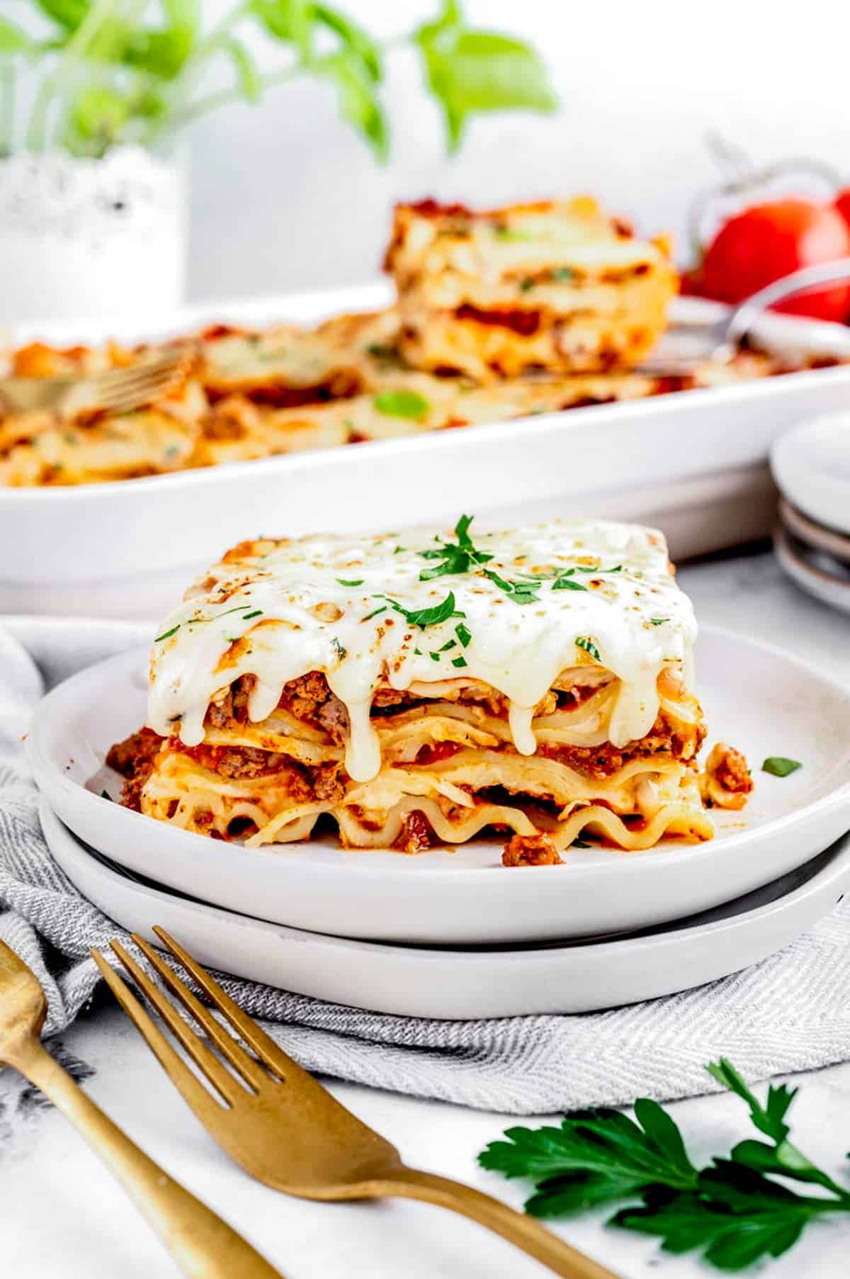 A slice of lasagna on two stacked plates with bechamel dripping down the sides.