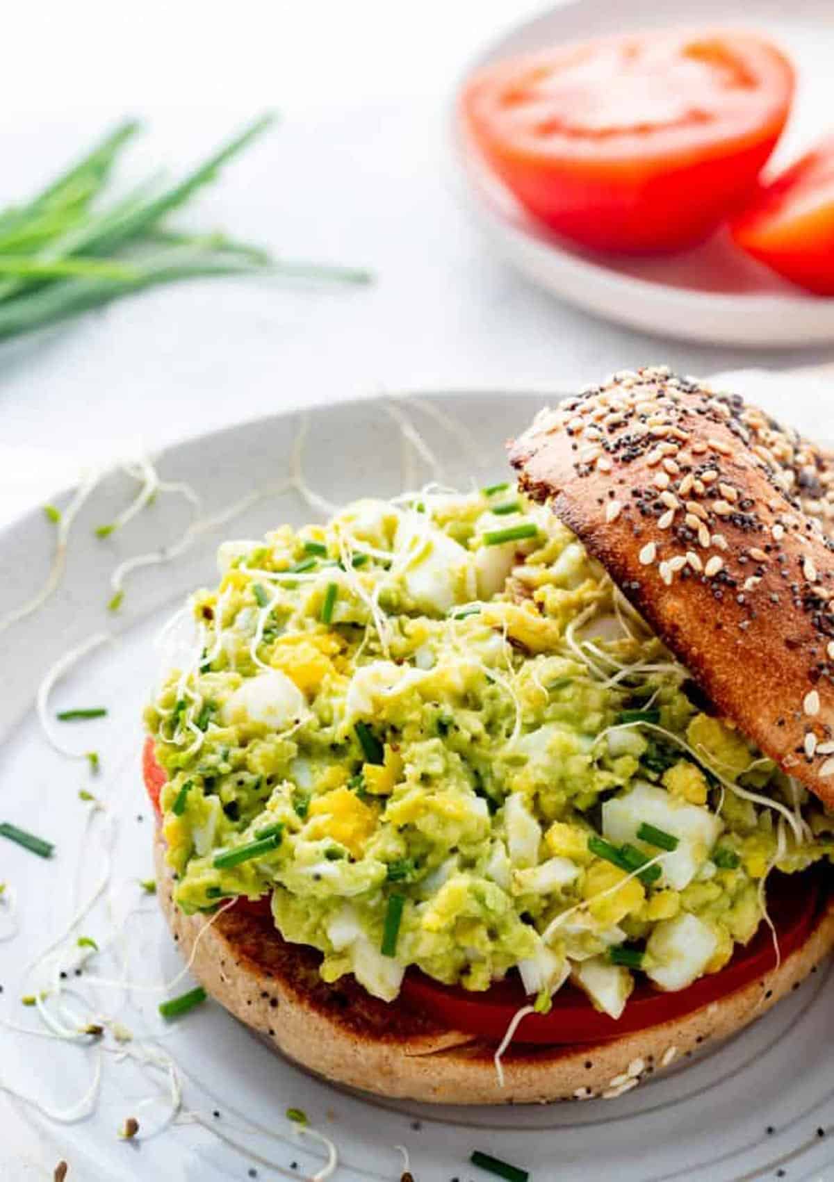 Avocado egg salad on a bagel with tomato slices.
