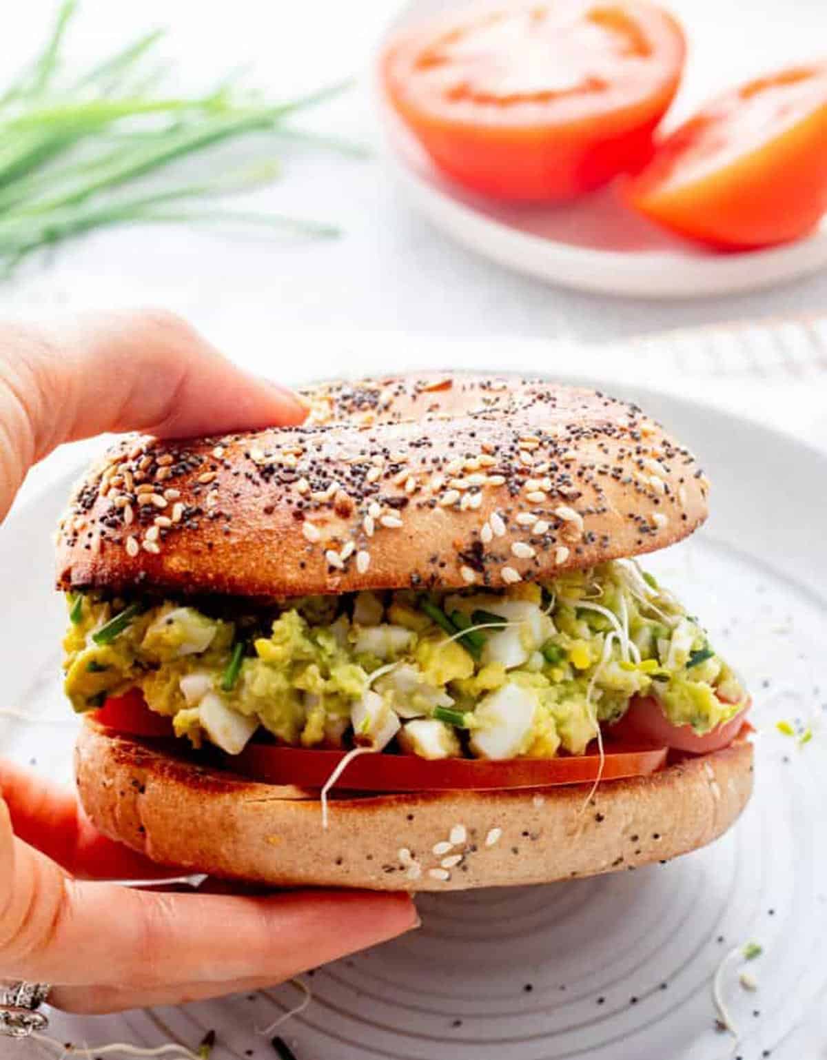 A hand holding bagel with avocado egg salad on it.
