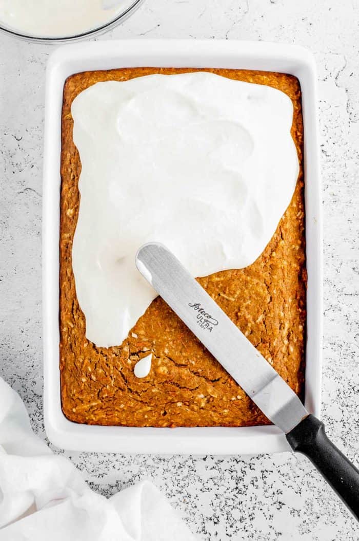 A large knife spreading the cream cheese frosting over the healthy carrot cake.