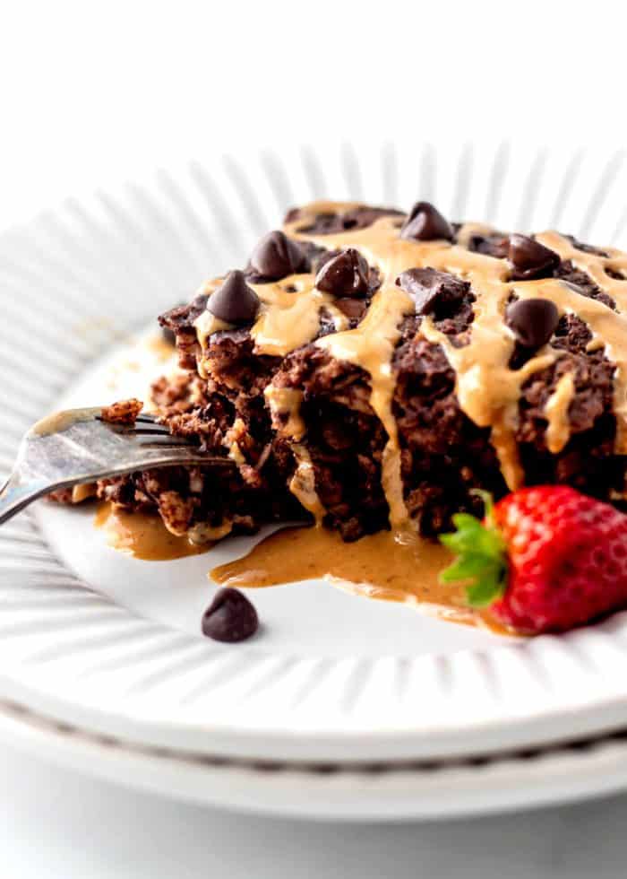 A slice of chocolate baked oats drizzled with peanut butter with a fork digging into it.